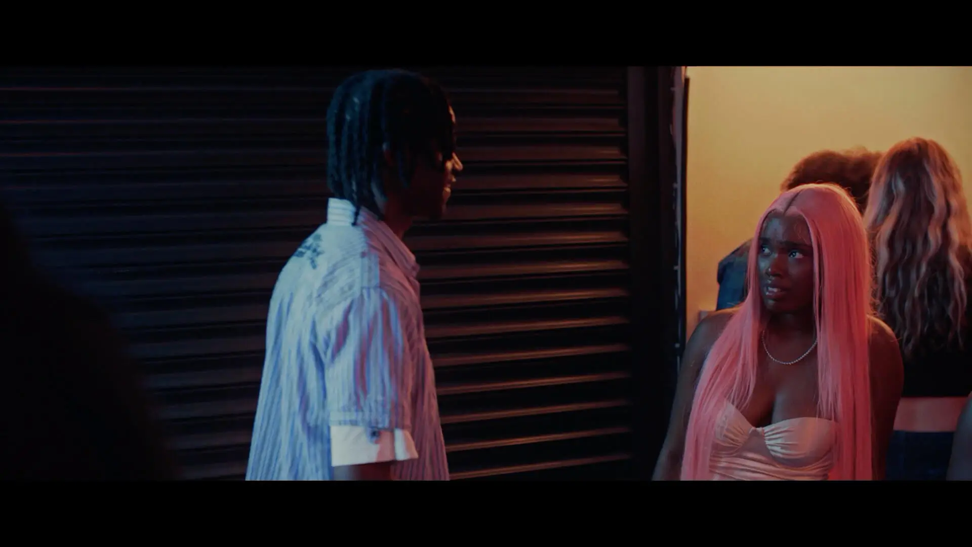 A man dressed smart being rejected by a woman in a dress with pink hair, from the film Till Dawn, talking at a party.