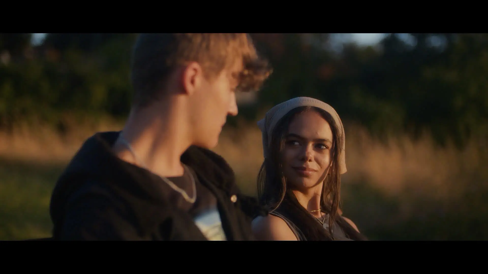 A man and woman, from the film Till Dawn, sitting on a bench in the park, having a conversation as the sun rises.